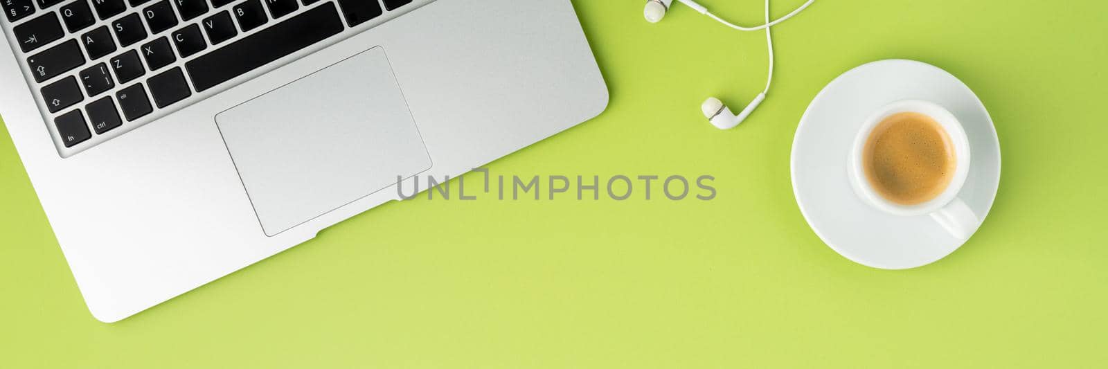 Banner of laptop keyboard, cropped white earphones, cup of espresso coffee on light green background. Modern workspace for study and business. Top view, copy space. Web page format