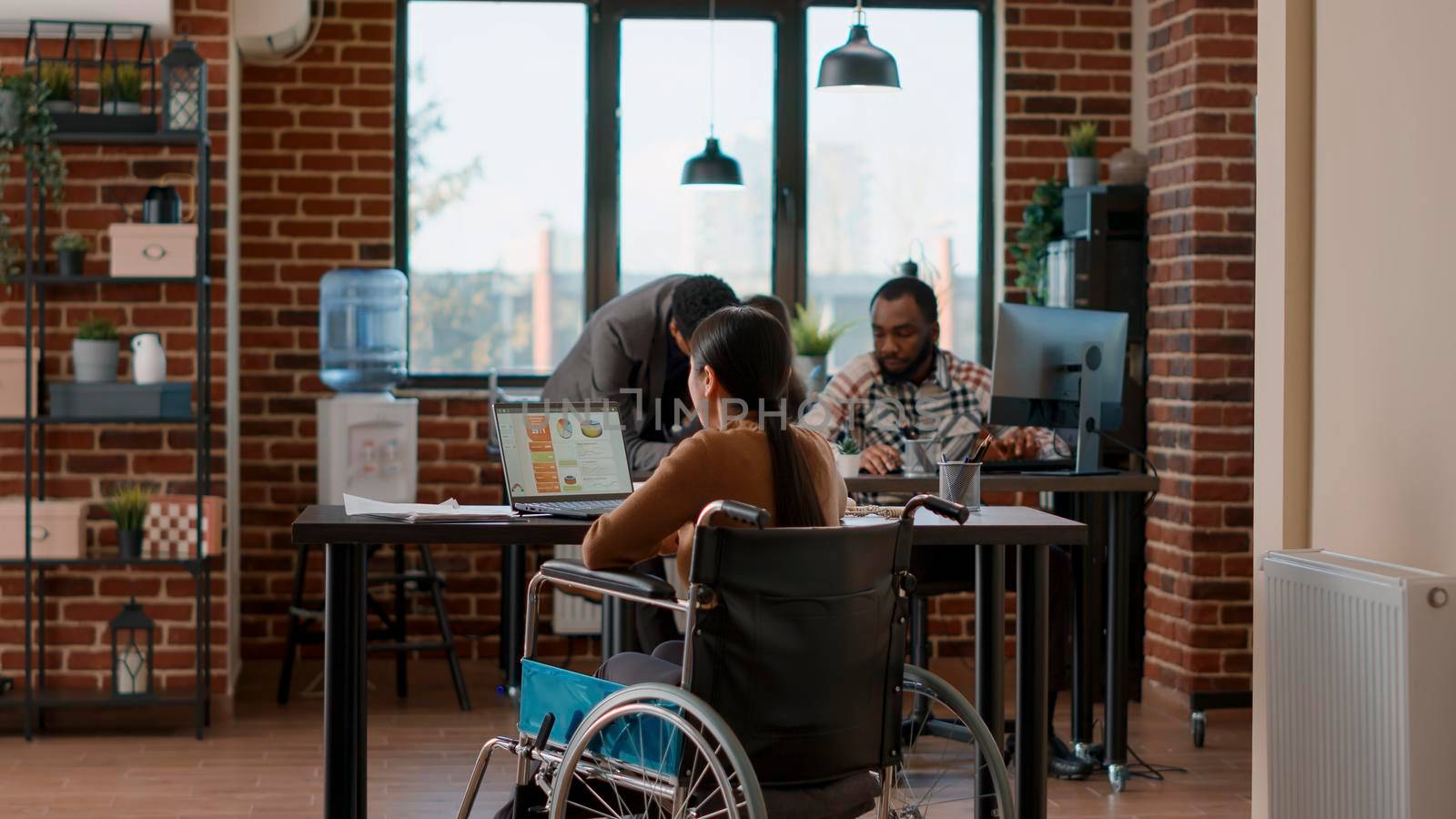 African american man helping woman in wheelchair with transportation, entering office job. Person with impairment working on business charts development, planning financial strategy. Tripod shot.