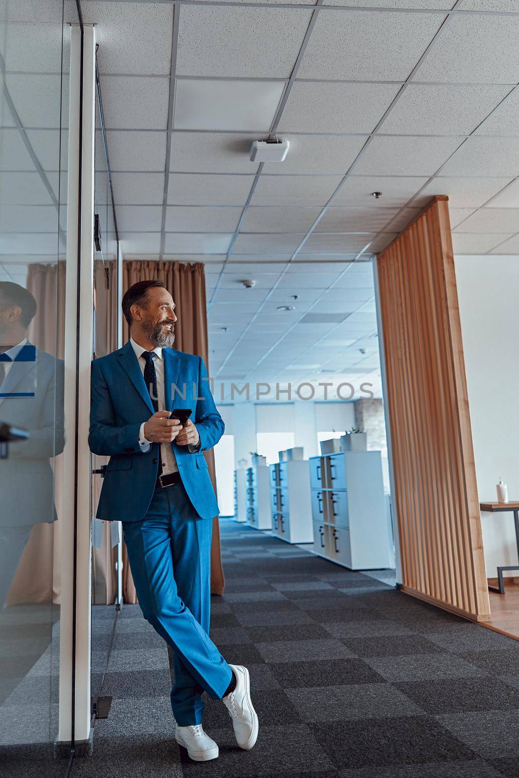 Smiling man standing, holding mobile phone and looking away by Yaroslav_astakhov