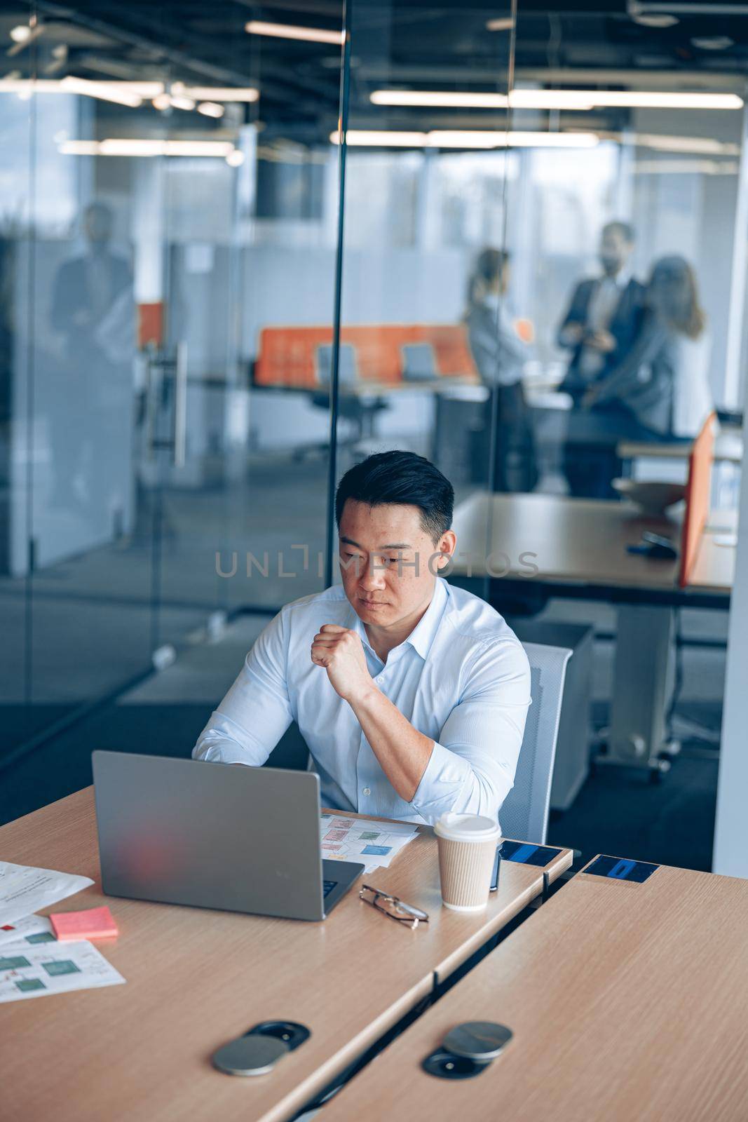 asian businessman working on laptop in office with colleagues in the background. Business concept