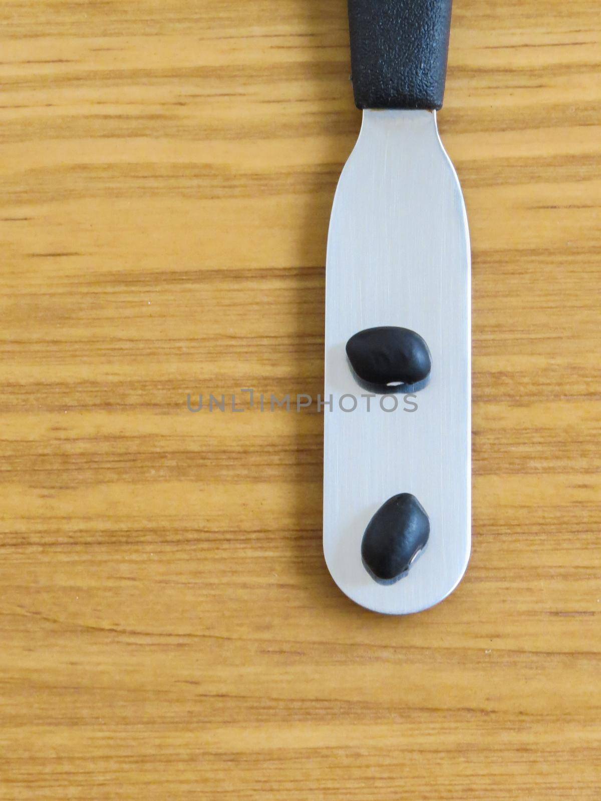 A close-up of a spatula with two black beans on a wooden textured background.