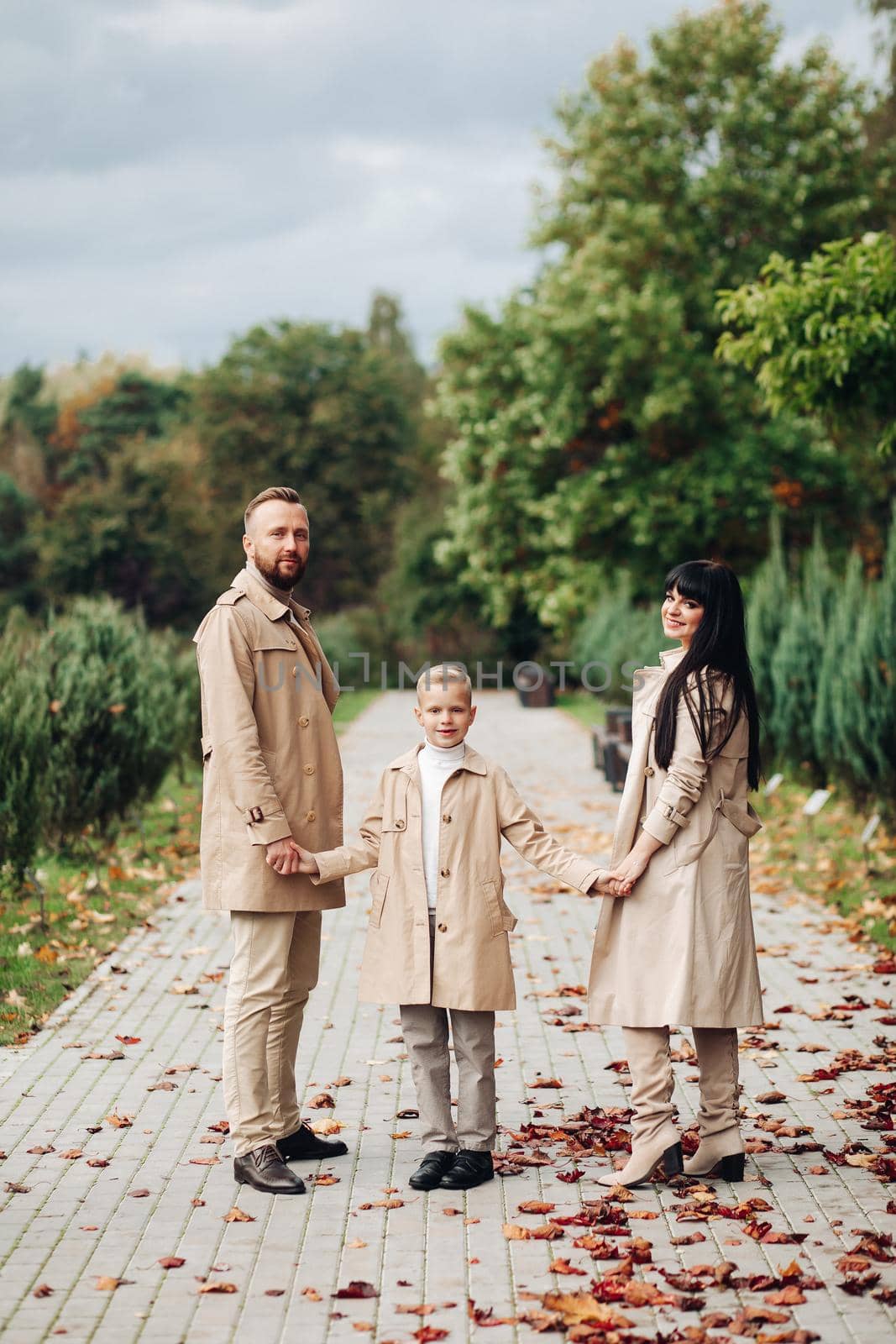 A happy family is walking in the park. Mom, dad and son are chatting and walking. A stylish family. parents in love. by StudioLucky