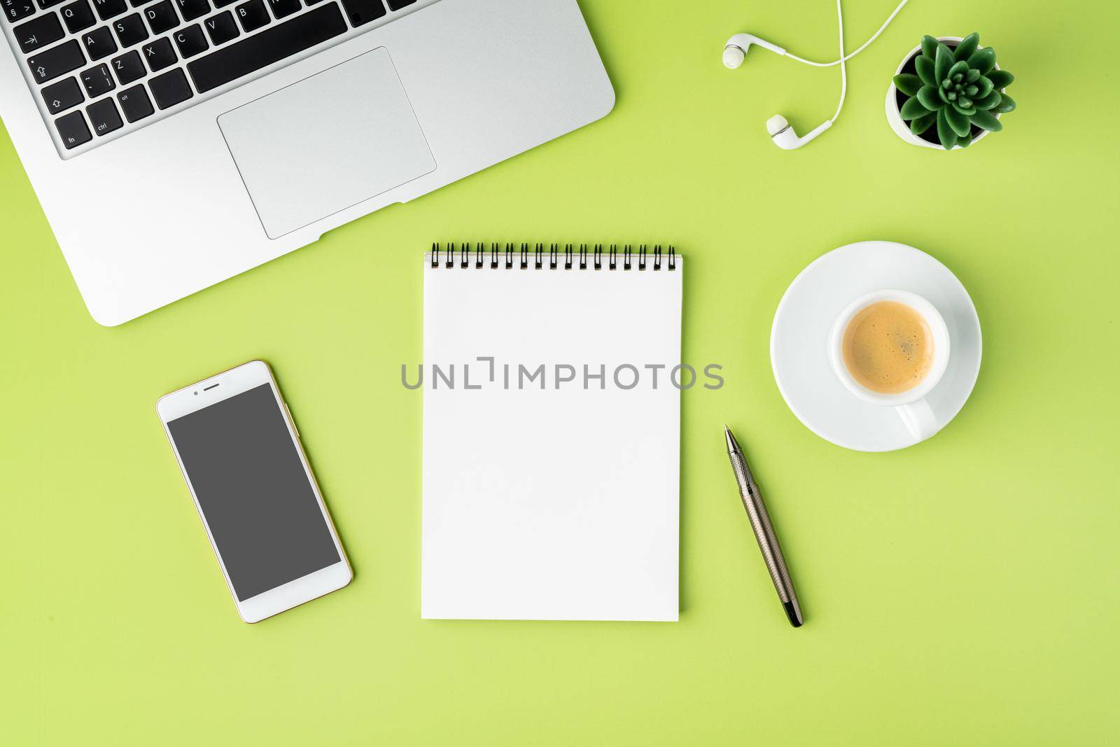 Concept of modern workspace. Notebook, smartphone, coffee cup, laptop and earphones on green backdrop by NataBene