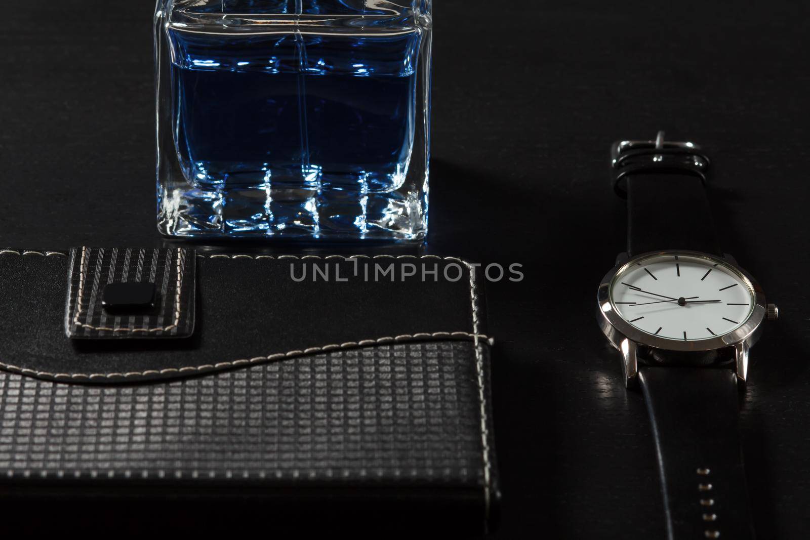 Man perfume, watch with a leather strap, notebook in leather cover on a black background