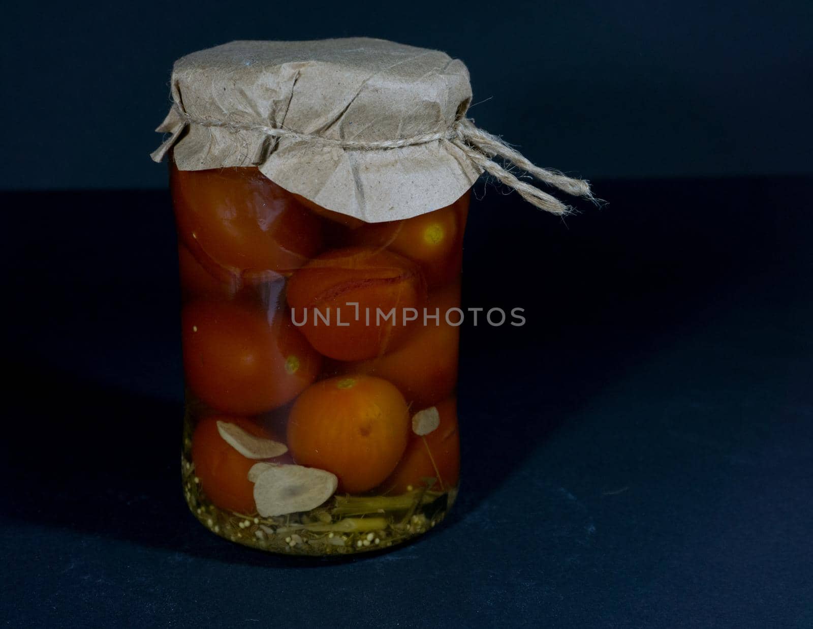 A jar of pickled red tomatoes on a black background.