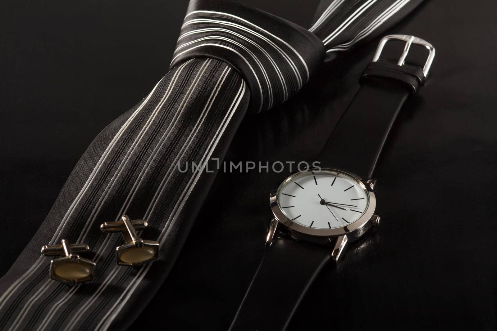 Silk tie, cufflinks, watch with a leather strap on a black background