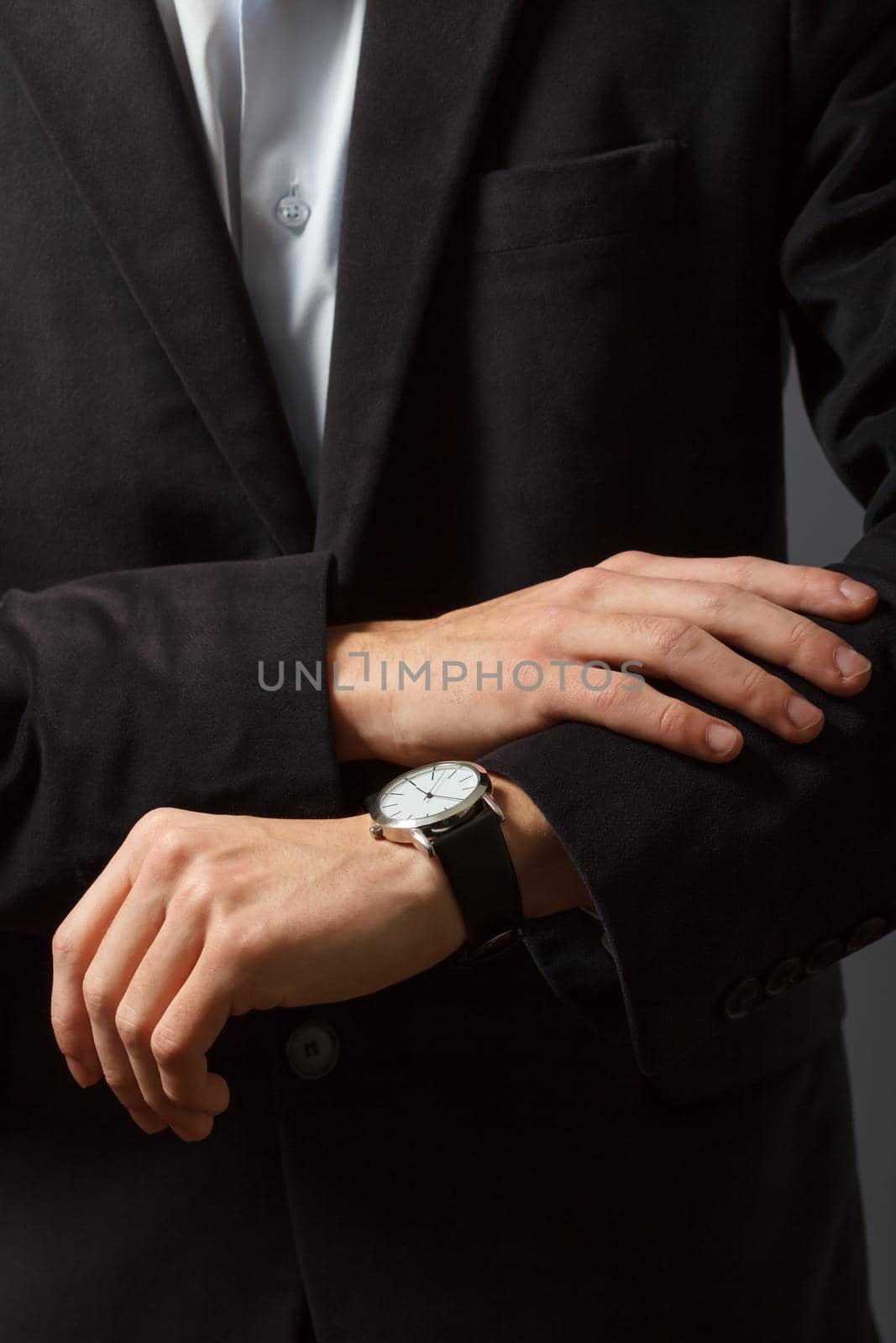 Young man in a suit is standing and looking at his watch