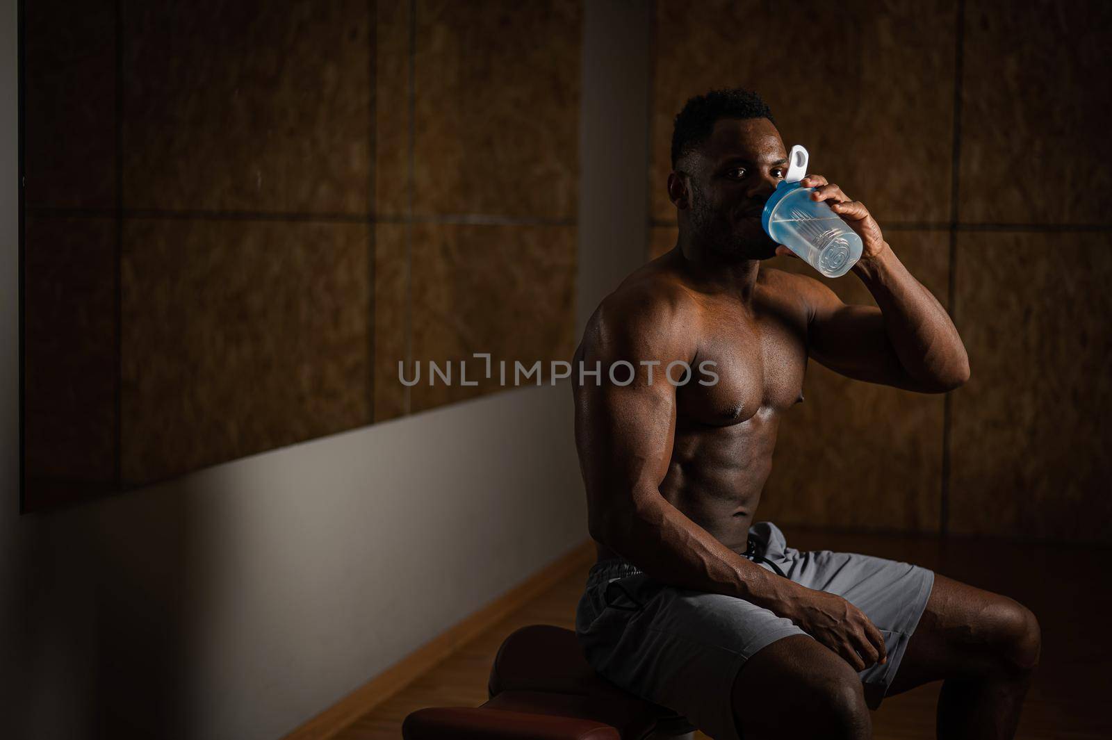 Shirtless african american man drinking from a shaker in the gym. by mrwed54