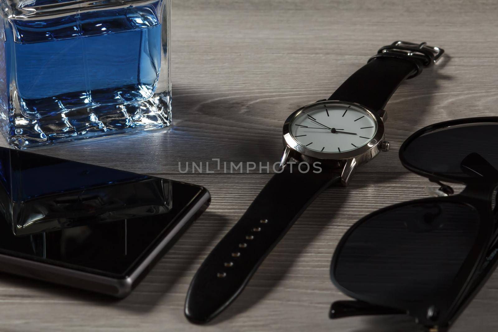 Man perfume, watch with a leather strap, sell phone, black sunglasses on a gray wooden background