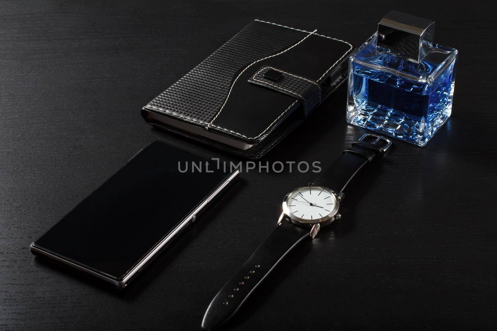 Watch with a leather strap, notebook in leather cover, sell phone, man perfume on a black background