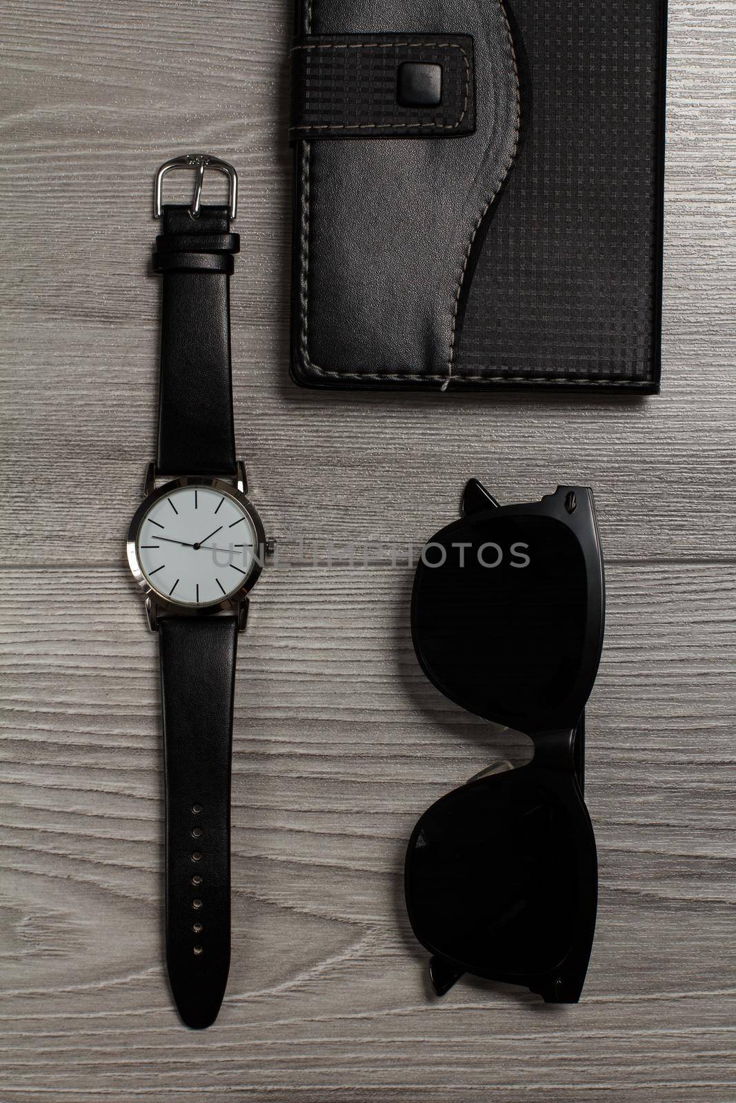 Watch with a leather strap, notebook in leather cover, black sunglasses on a gray wooden background