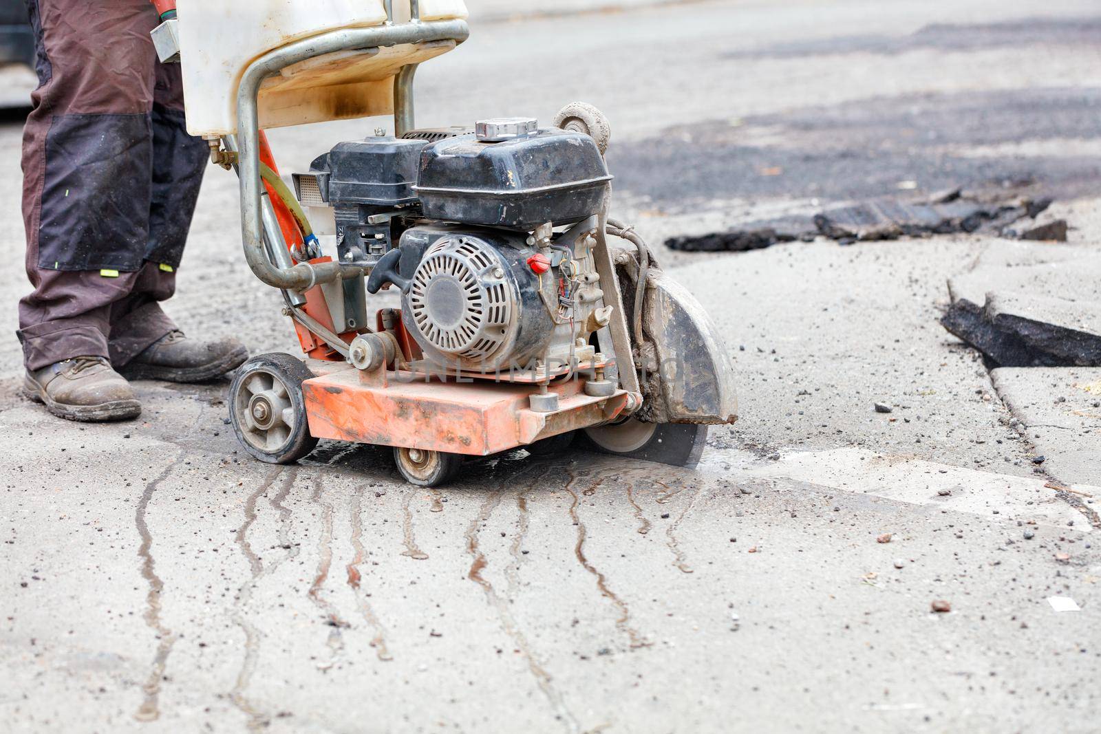 A worker cuts the asphalt with a diamond cutting disc using a petrol cutter. by Sergii