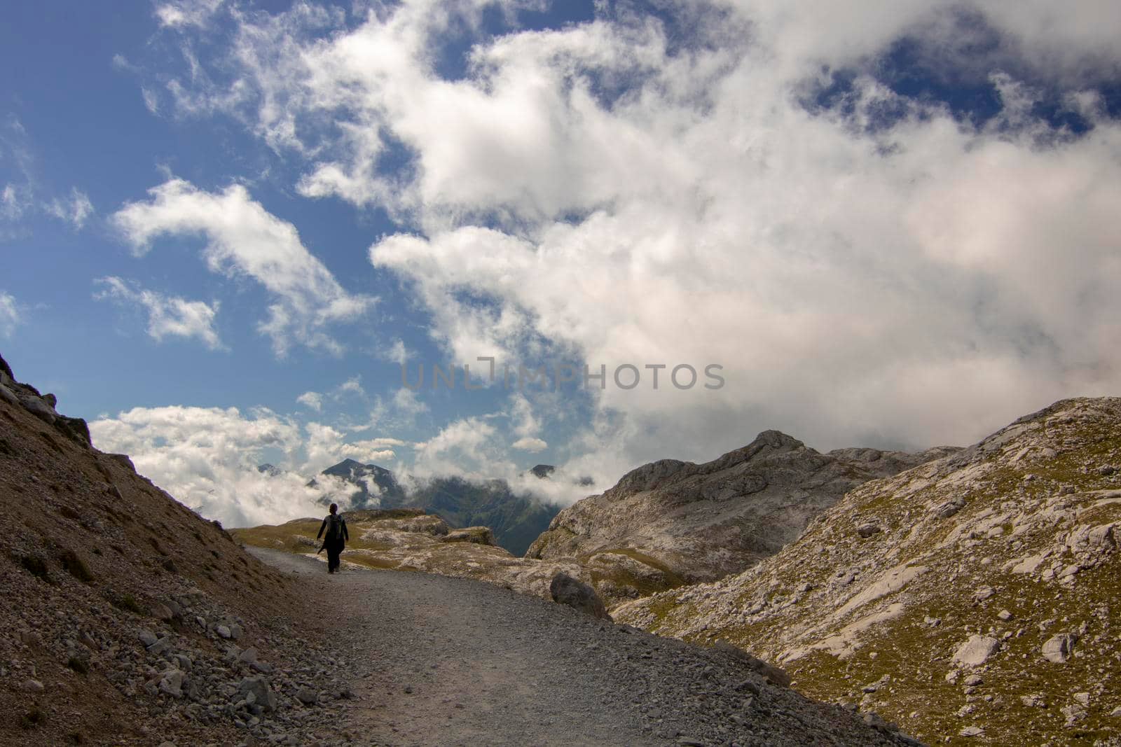 A girl walking on a path surrounded by some mountains under some clouds in a beautiful landscape in Fuente De in Spain