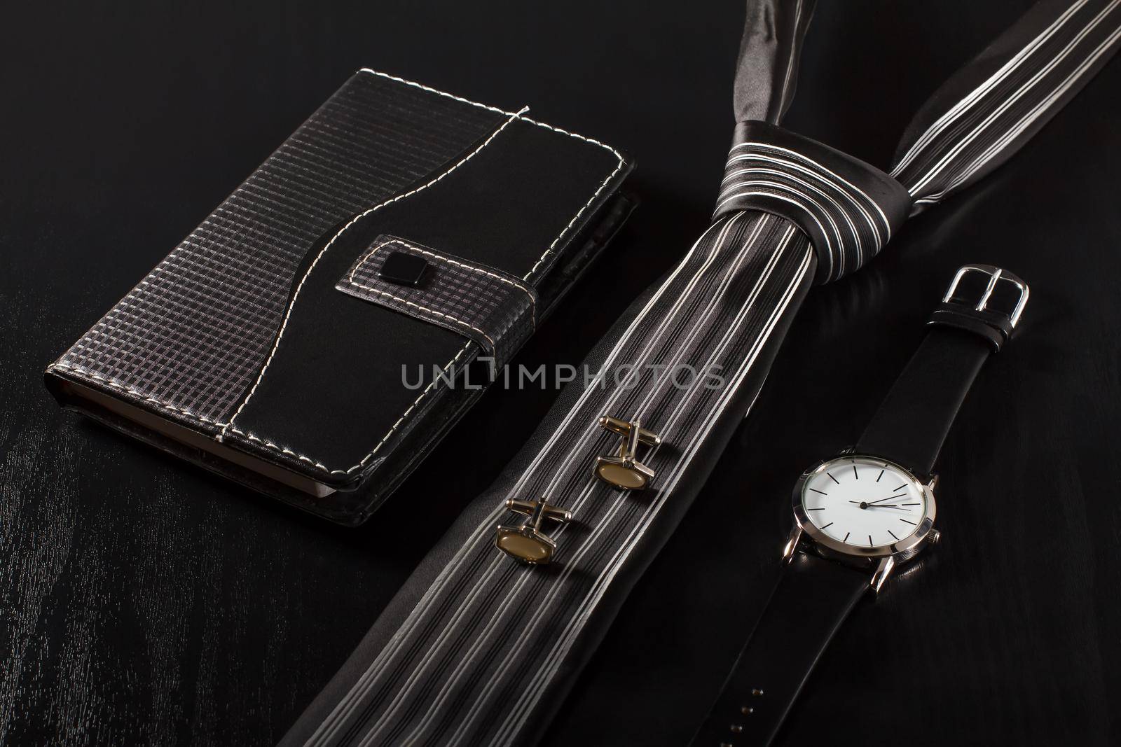 Notebook in leather cover, tie, cufflinks, watch with a leather strap on a black background