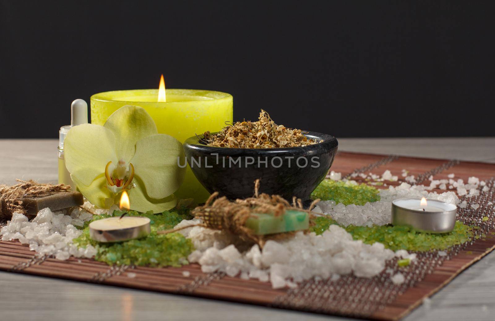 Spa accessories with soap, orchid flower, bowl with dried chamomile flowers, bottles with aromatic oil, sea salt, candles on bamboo napkin