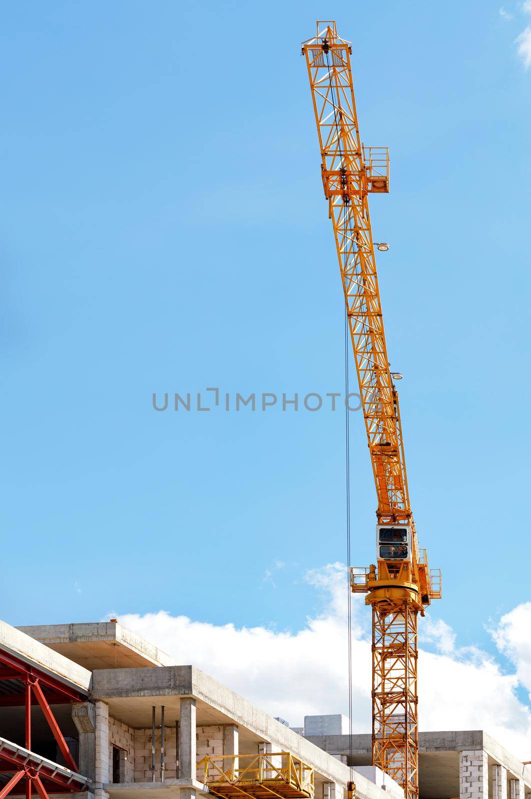 A tower crane jib leaps up over a construction site against a clear blue sky, vertical image, copy space.