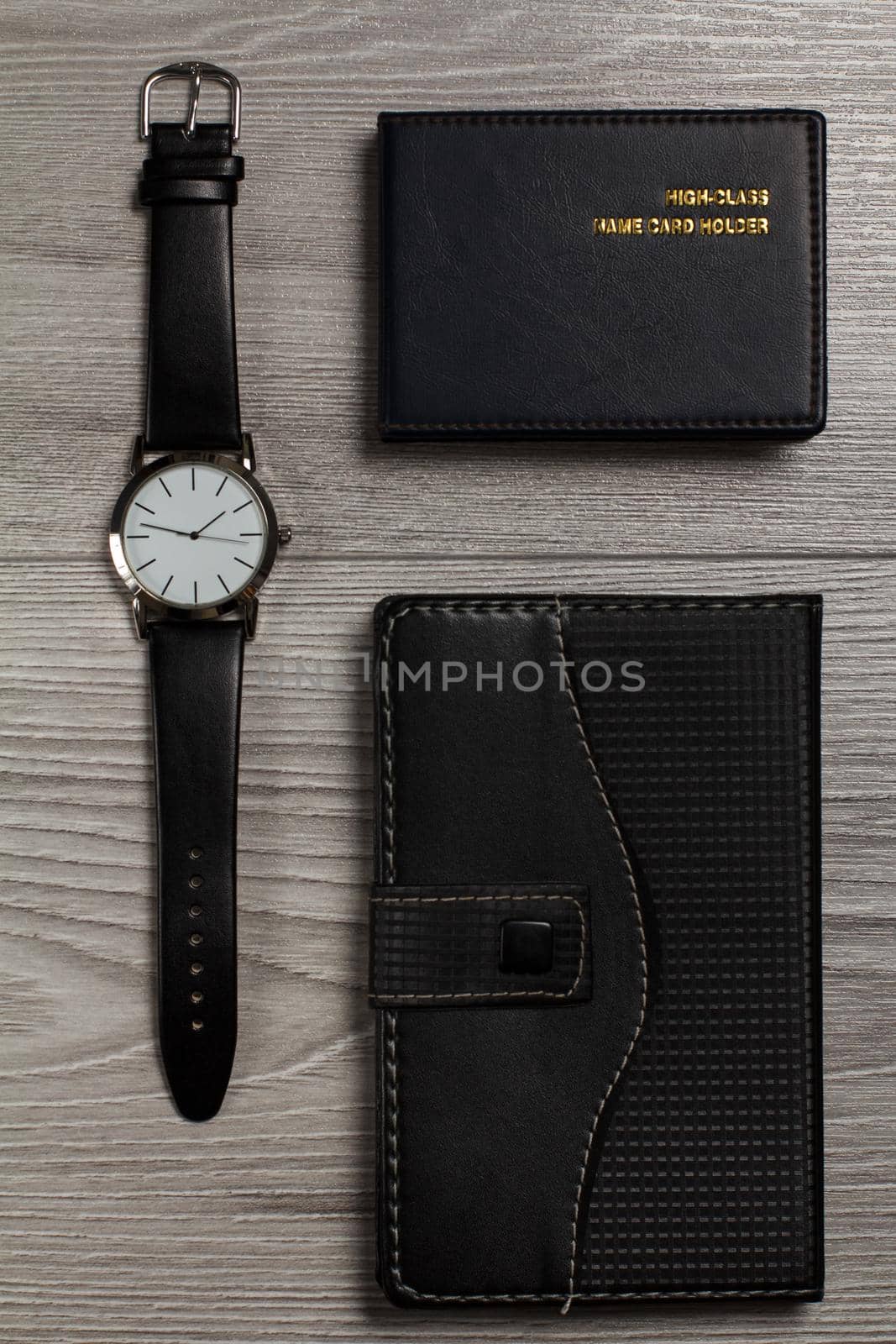 Watch with a leather strap, notebook in leather cover, name card holder on a gray wooden background