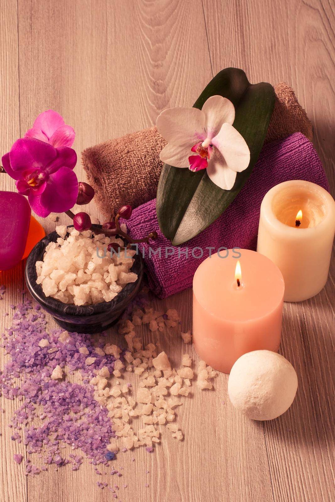 Spa setting with orchid flowers, bowl with sea salt, candles, soap and towels on wooden board