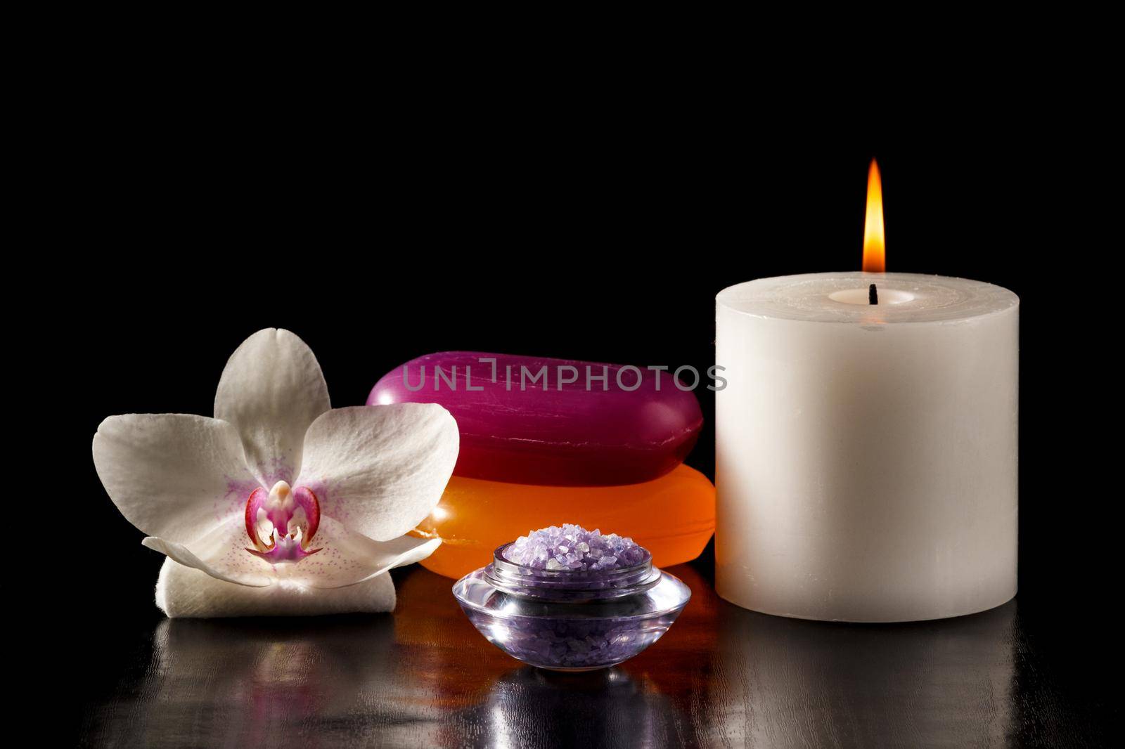 White orchid flower, soap, bowl with sea salt for spa, candle on black background