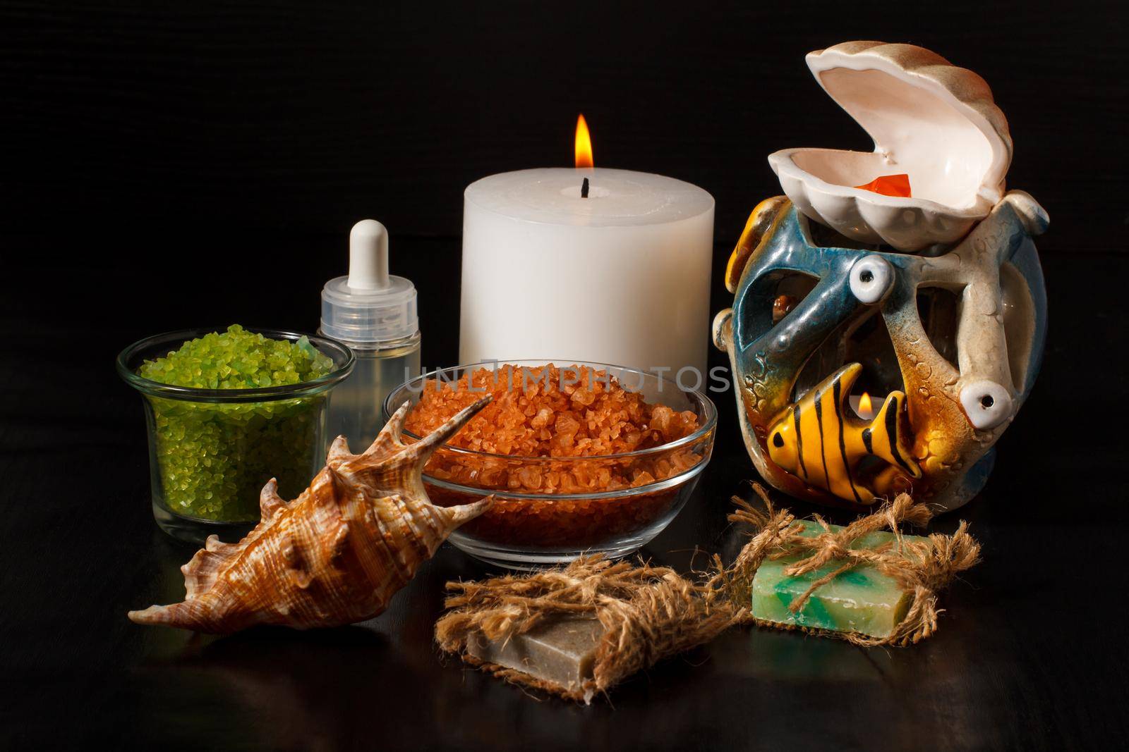 Spa products with handmade soap, bowls with sea salt, bottle with aromatic oil, candles and shell on black background