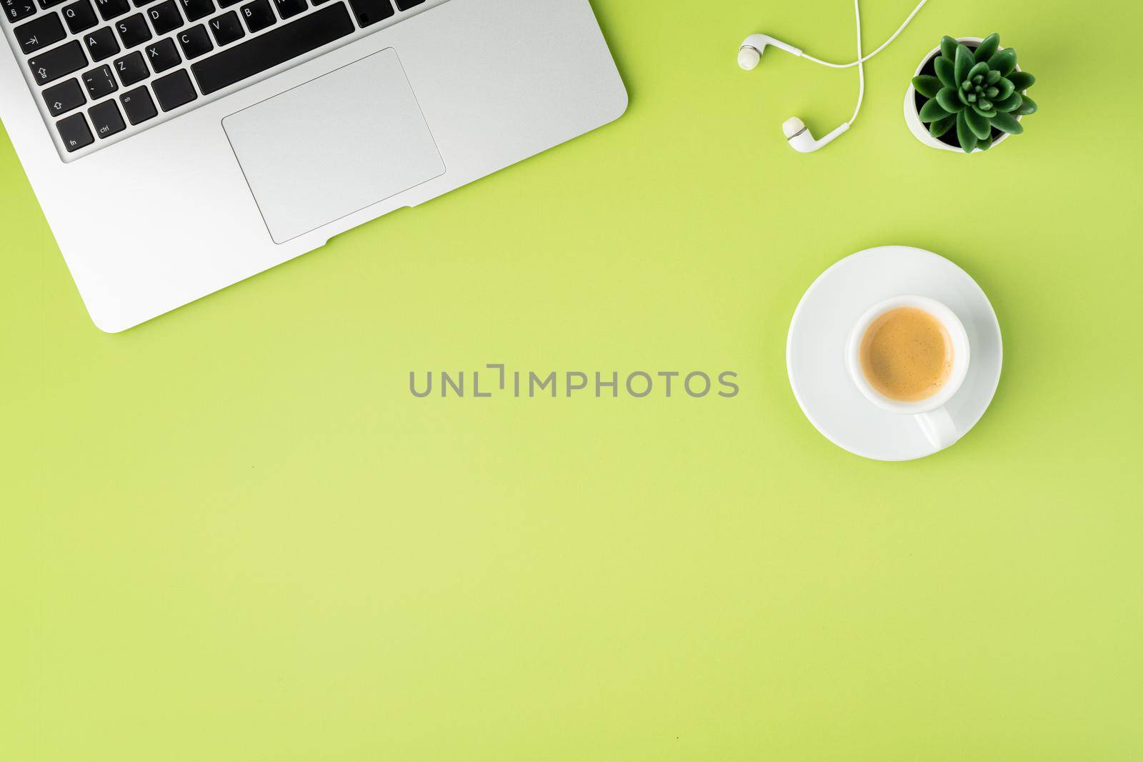 Horizontal of laptop keyboard, cropped white earphones, cup of espresso coffee on light green background. Modern workspace for study and business. High angle view, copy space