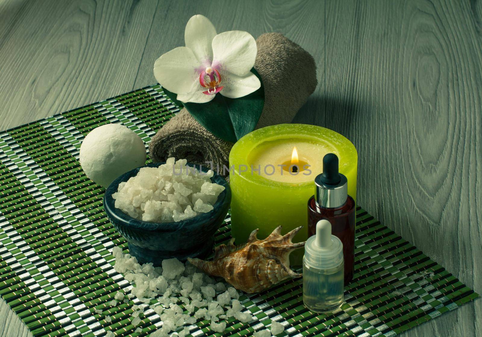Spa and wellness setting with orchid flower, bowl with sea salt, seashell, bottles with aromatic oil, candle and towel on bamboo napkin