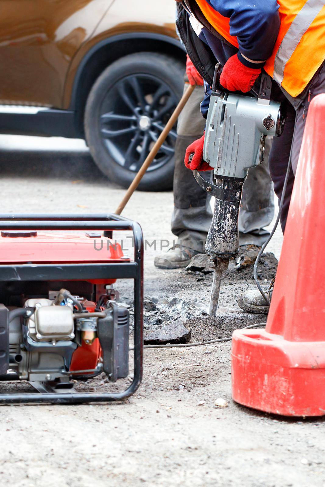 A team of road workers are repairing a section of the road with an electric jackhammer, petrol generator and shovel. by Sergii