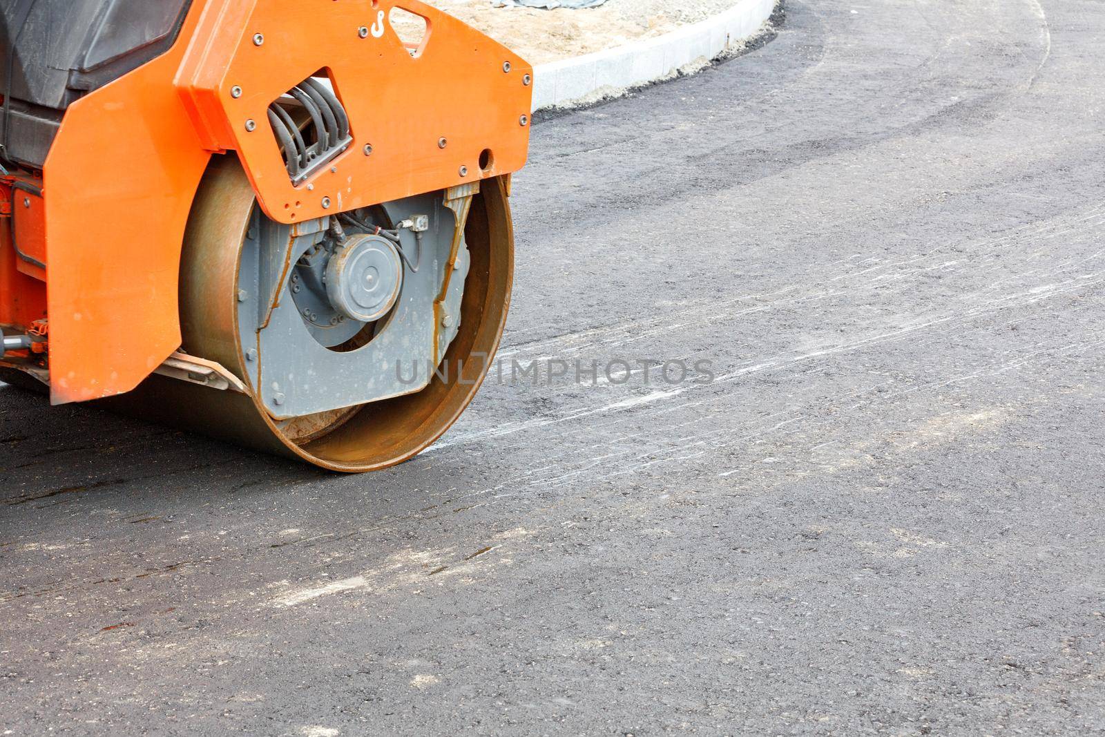 The metal cylinder of a large vibratory roller powerfully compacts the fresh asphalt of the road surface. Close-up, copy space.