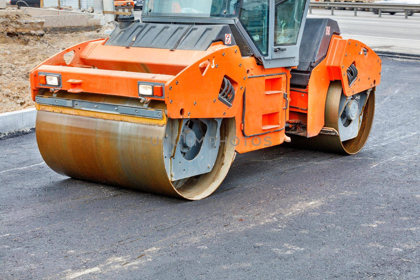 The metal cylinders of the large vibratory roller roll over the new road surface for powerful compaction of the fresh asphalt.