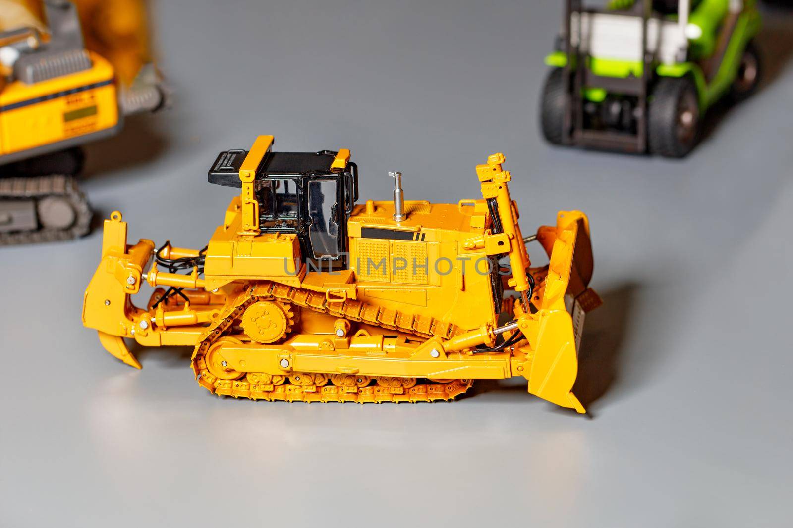 Toy model of a yellow construction bulldozer on a light gray background, selective focus, copy space.