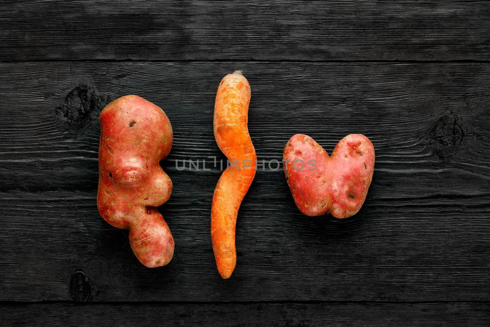 Beautifully deformed vegetables, ugly funny potatoes in the shape of a heart and letters and twisted carrots on a black wooden background. Waste prevention concept top view. Top view, copy space.
