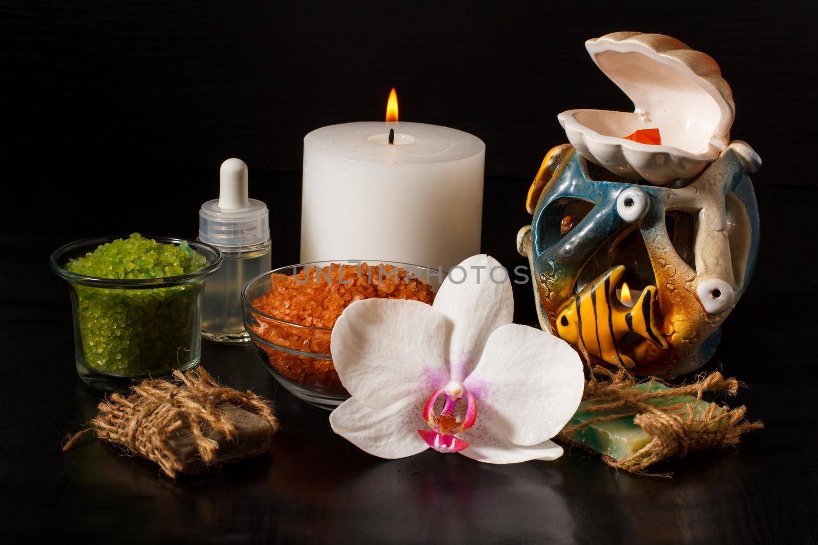 Spa products with orchid flower, handmade soap, bowls with sea salt, bottle with aromatic oil, candles on black background