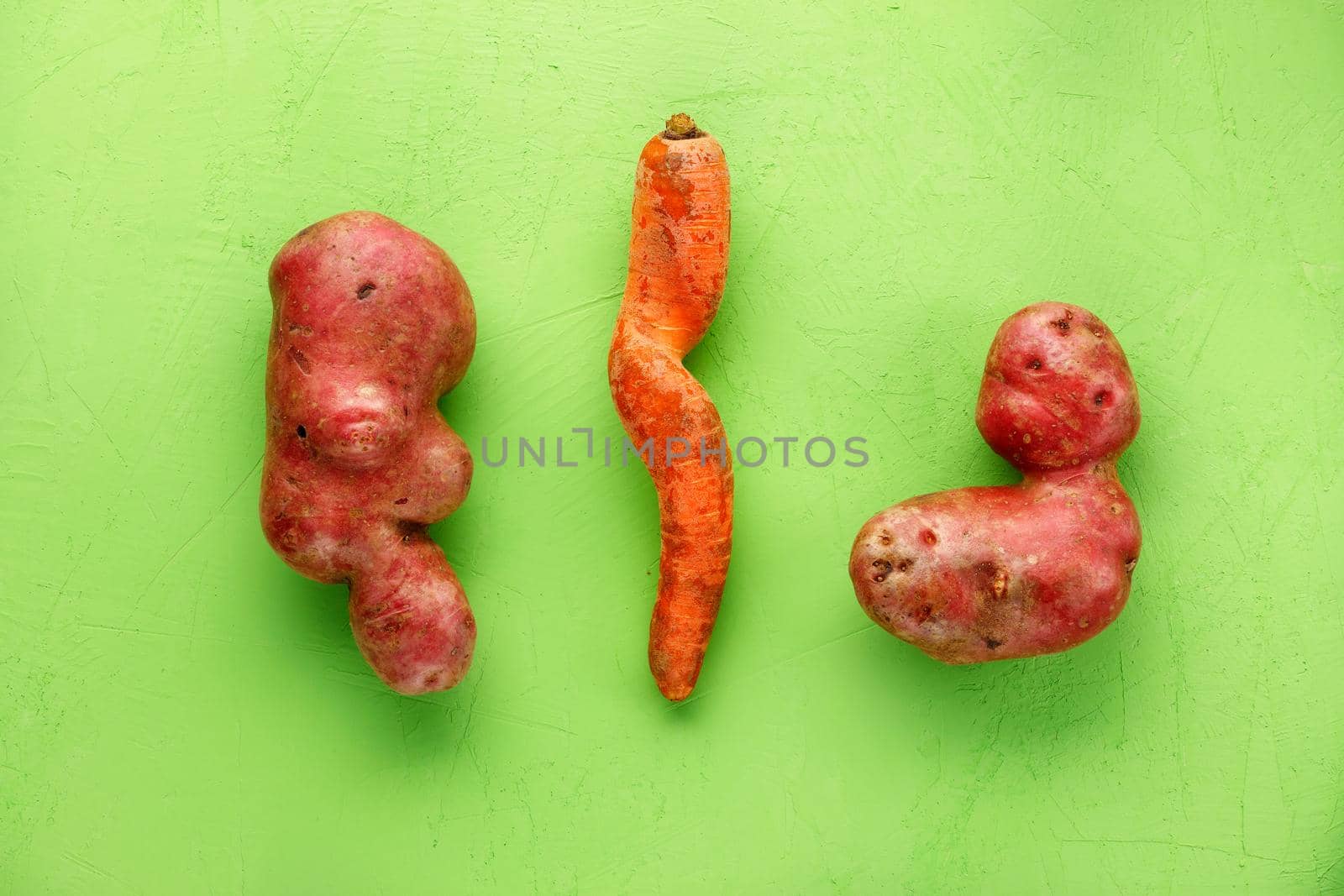 Ugly potatoes and carrots on a green background. Vegetable or food waste concept. Top view, close-up. by Sergii
