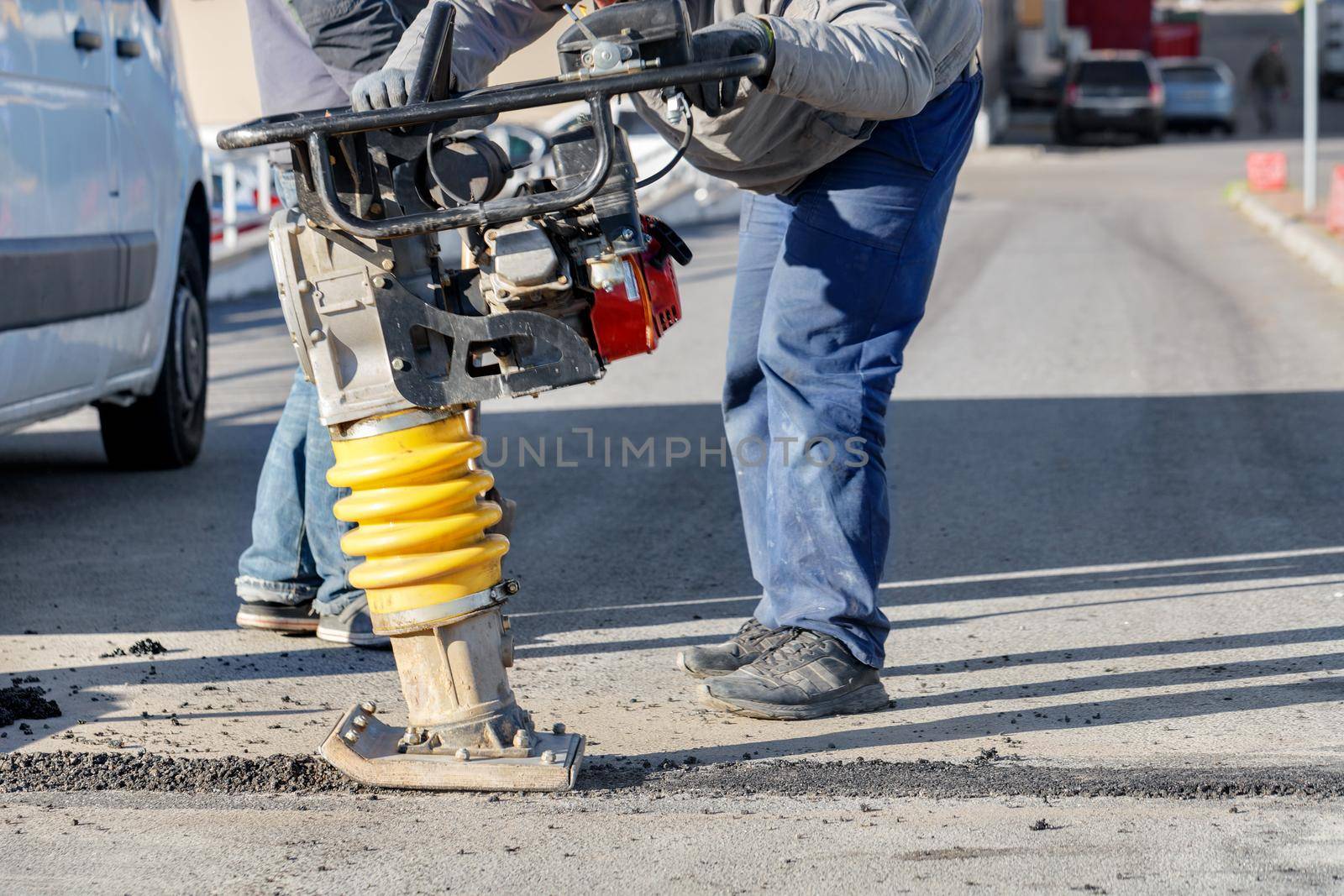 Road service workers use a petrol vibratory rammer to repair a section of the road. by Sergii