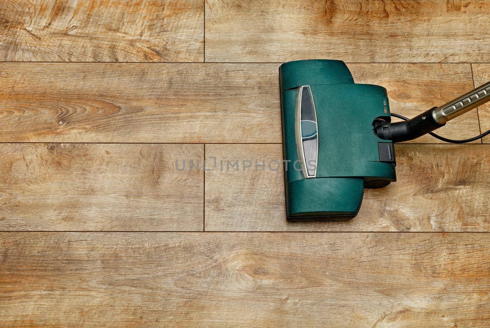 The brush of an electric vacuum cleaner on the background of a brown floor from a wooden floor board. by Sergii