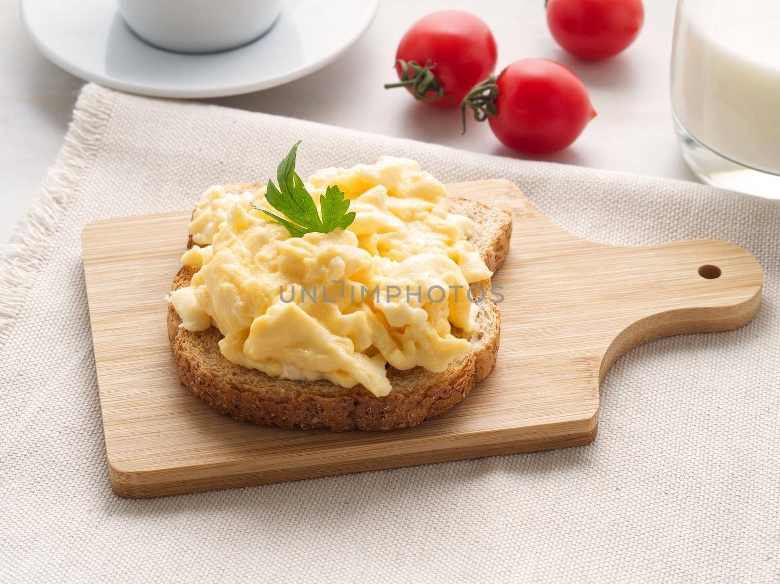 Sandwich with pan-fried scrambled eggs on a wooden cutting board, side view.