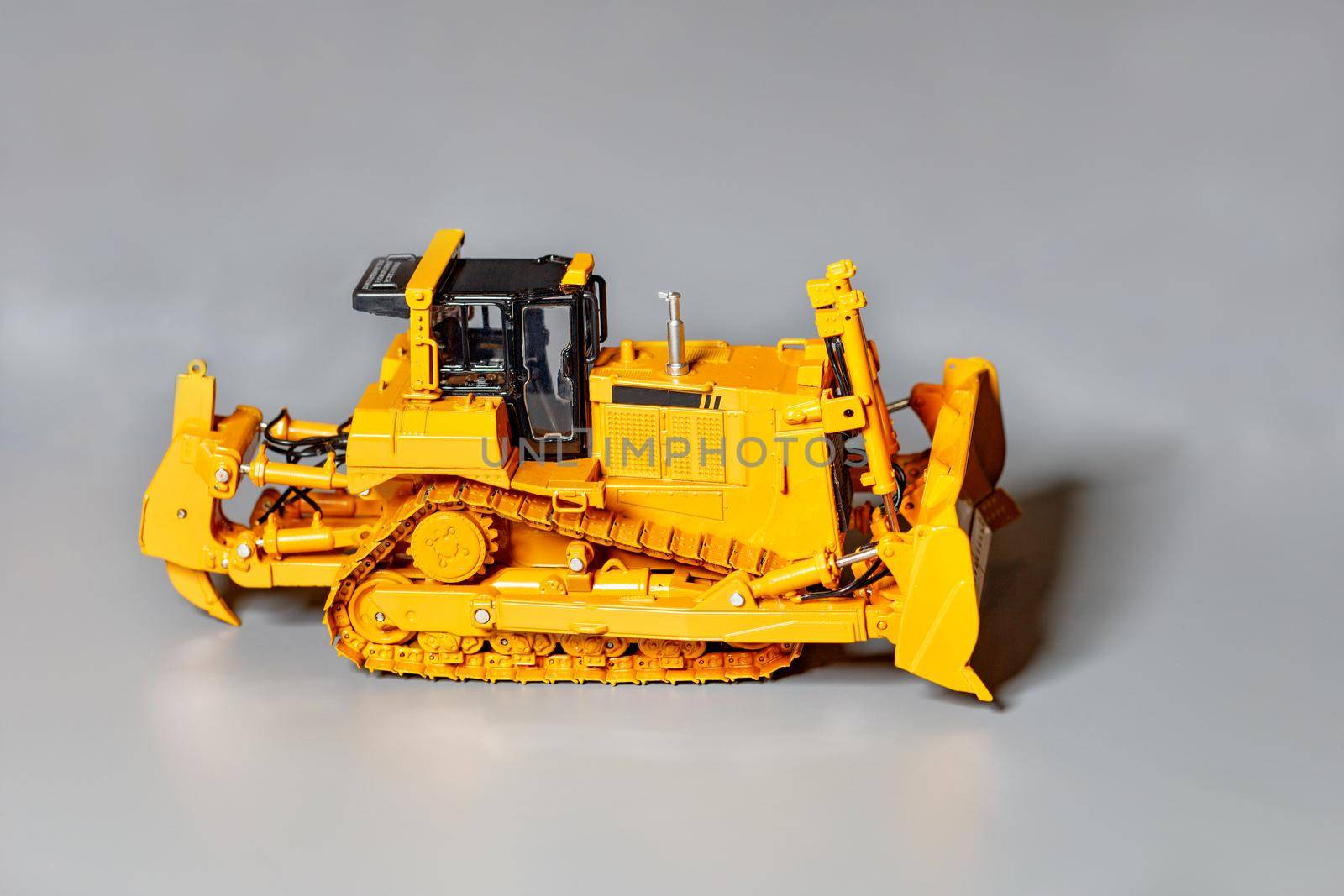 Toy model of a yellow color bulldozer on a light gray background, selective focus, copy space.