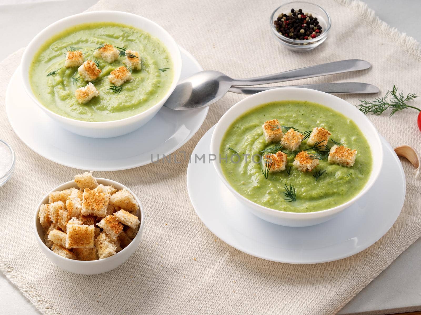 Two large white bowl with vegetable green cream soup of broccoli, zucchini, green peas on a white background, side view