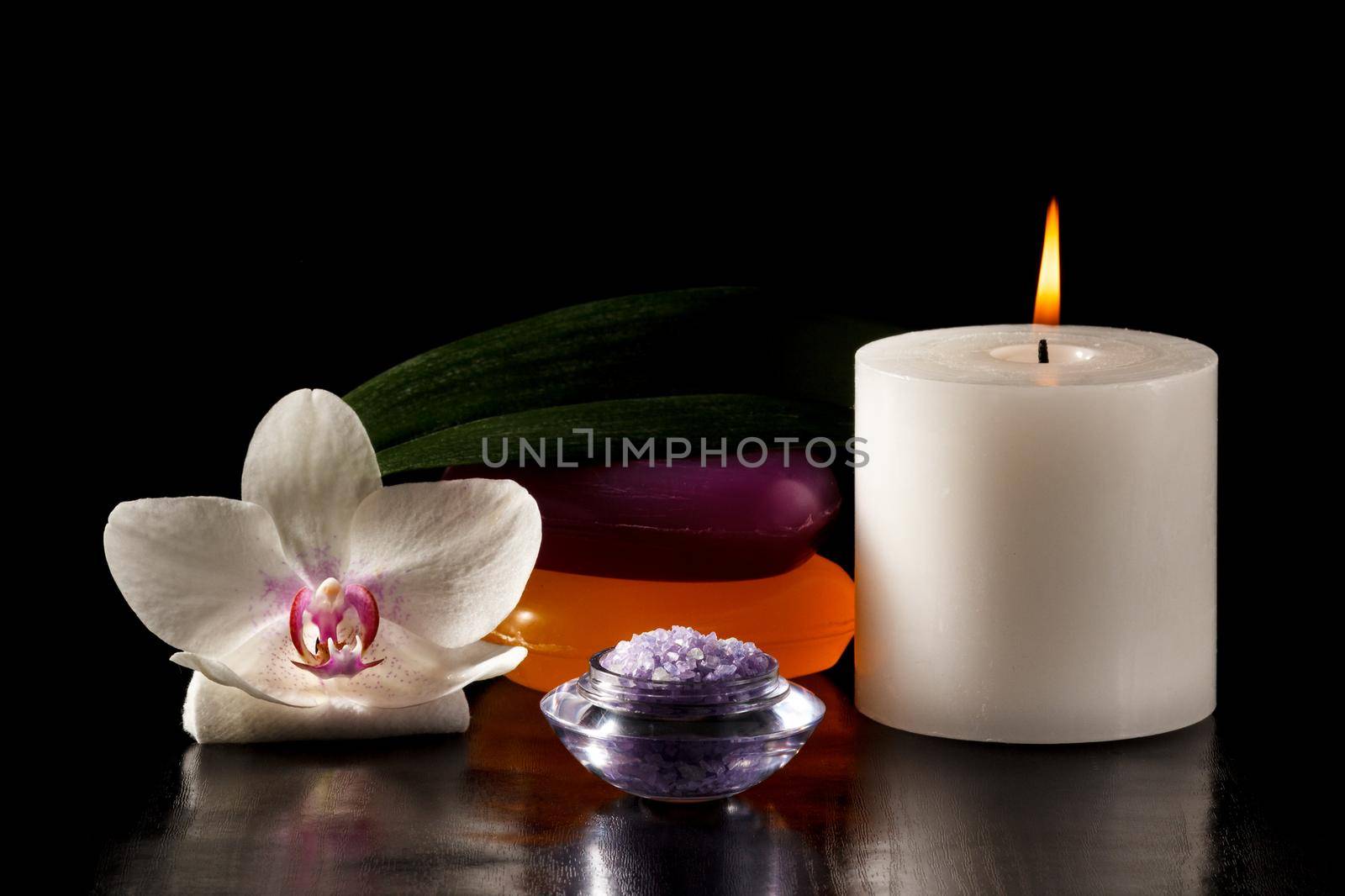Orchid flower, soap, bowl with sea salt for spa, candle on black background