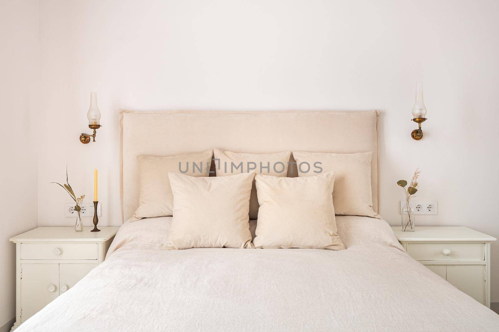 Bright bedroom interior, cozy bed with beige linen, dry flowers on a bedside table
