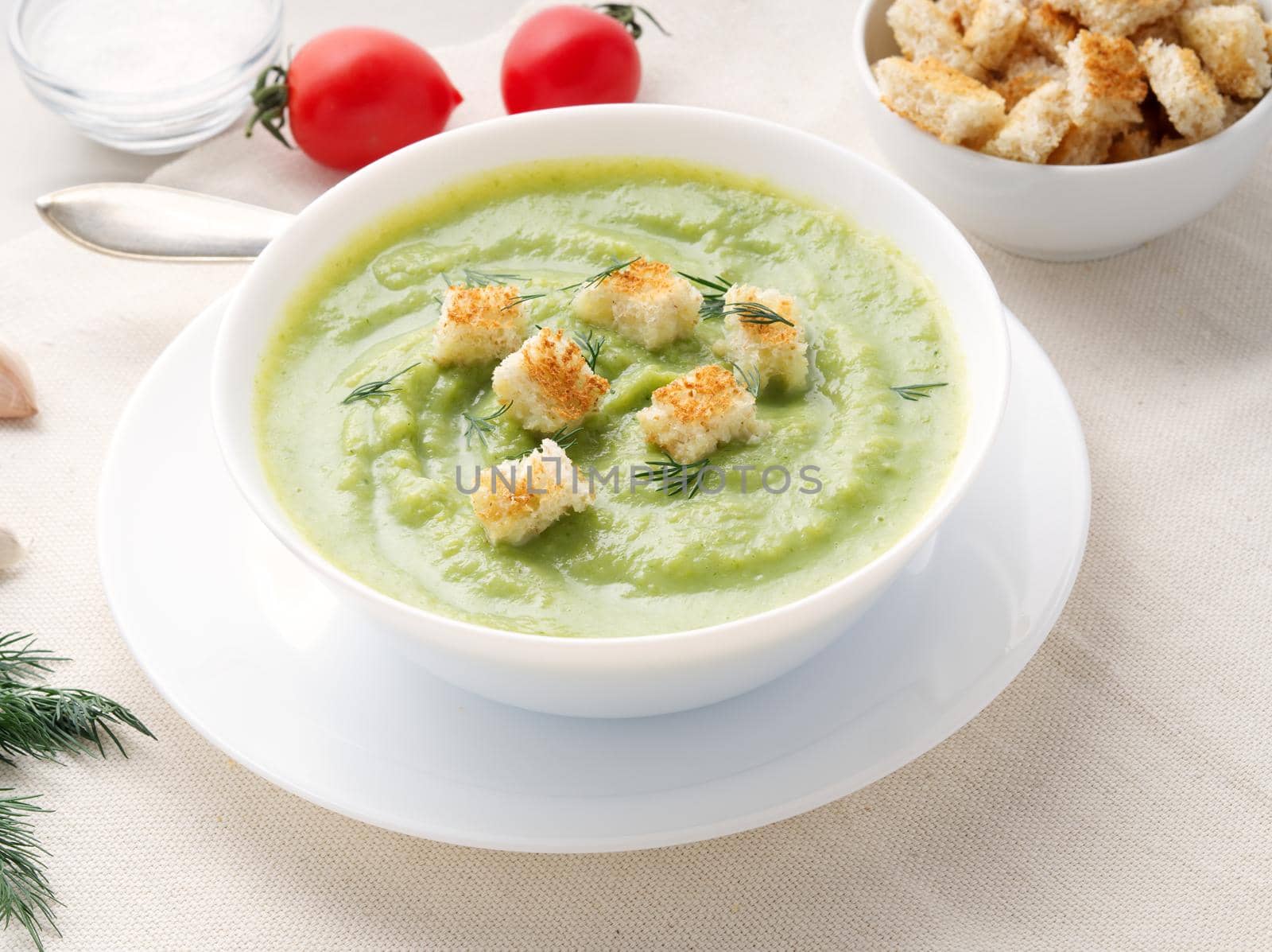 large white bowl with vegetable green cream soup of broccoli, zucchini, green peas on a white background, side view