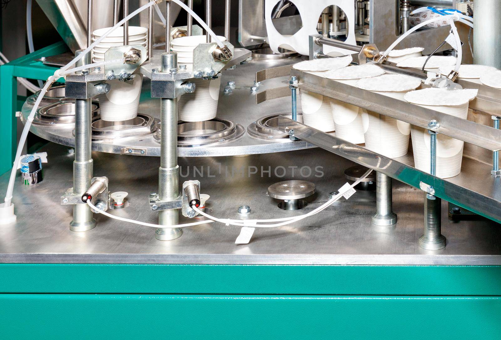 Fragment of the production line for the filling and packaging of yoghurts in paper cups, the concept of processing, storage and packaging of dairy products, close-up, copy space.