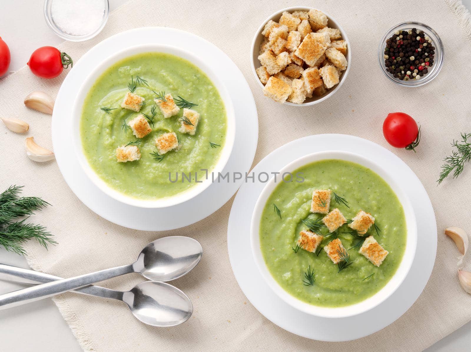 Two large white bowl with vegetable green cream soup of broccoli, zucchini, green peas on white by NataBene