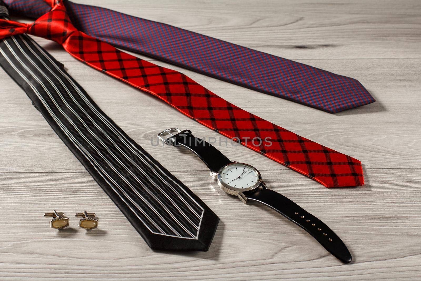 Color silk neckties, watch with a leather strap, cuff-links on a gray wooden background