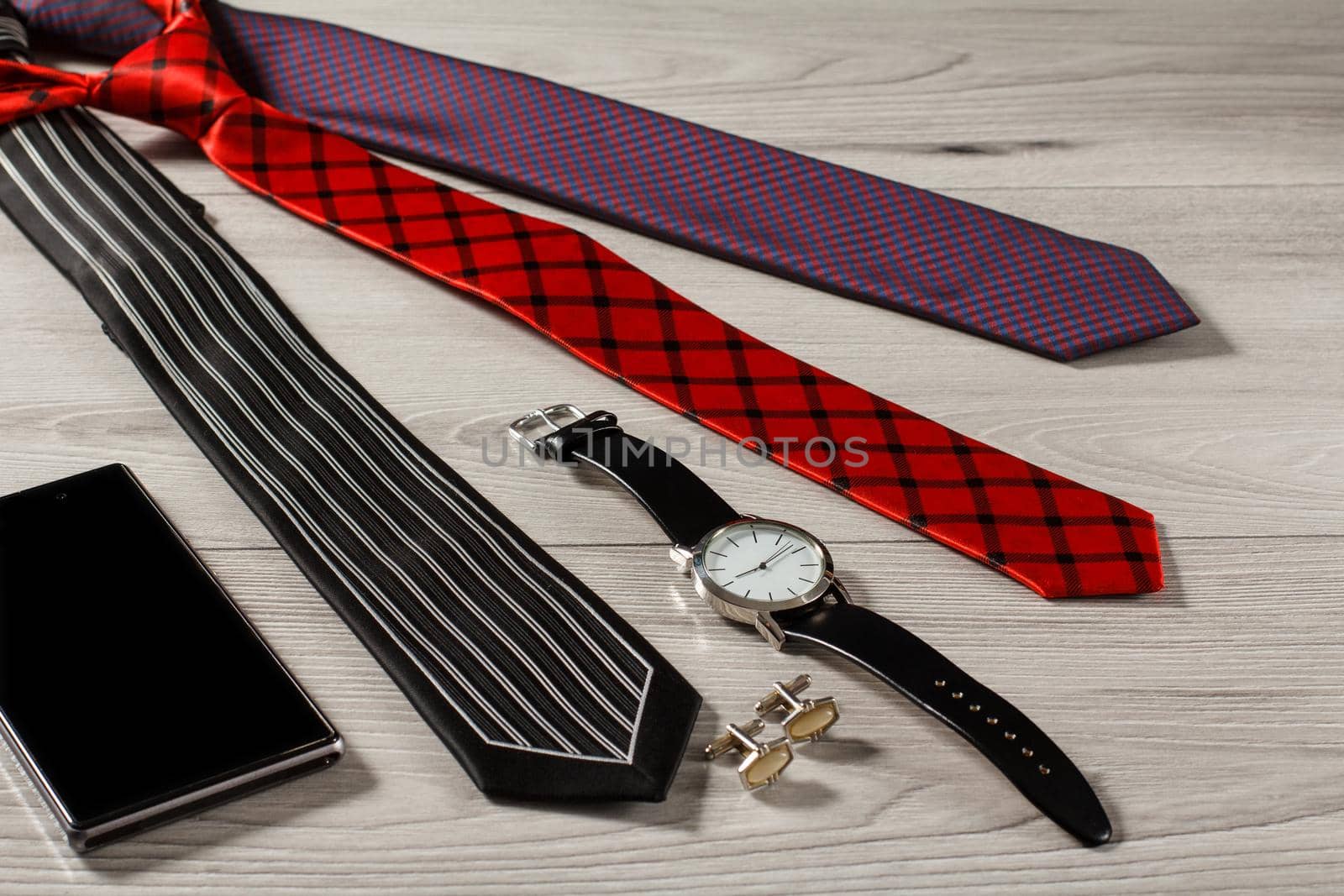 Color silk neckties, watch with a leather strap, cufflinks, sell phone on a gray wooden background