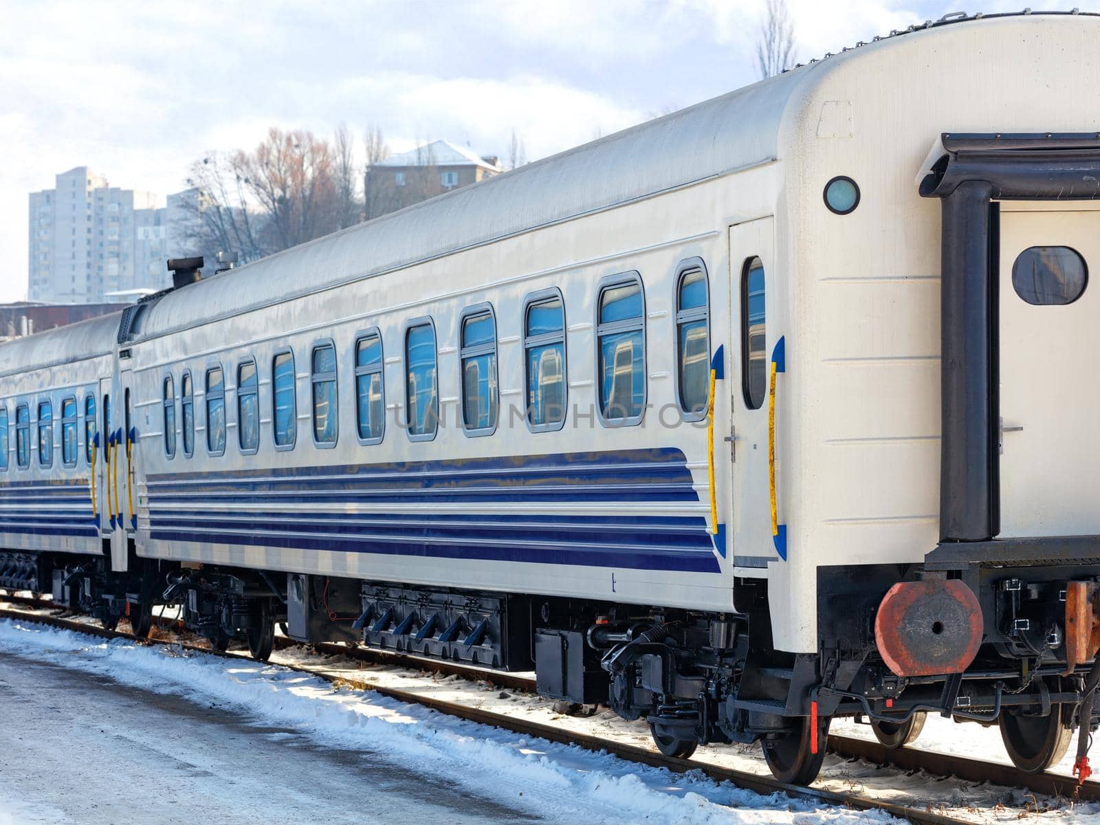 A white railroad car with blue stripes stands on the tracks on a bright sunny winter day.