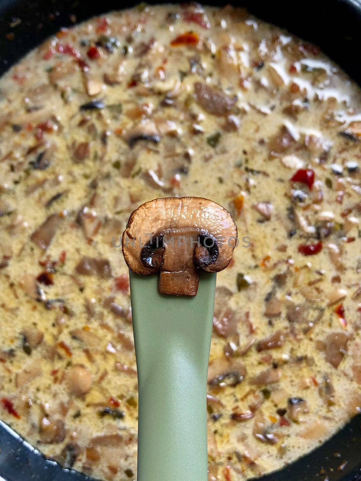 Single fried mushroom on spatula over the pan with white sauce. Trying the product while cooking