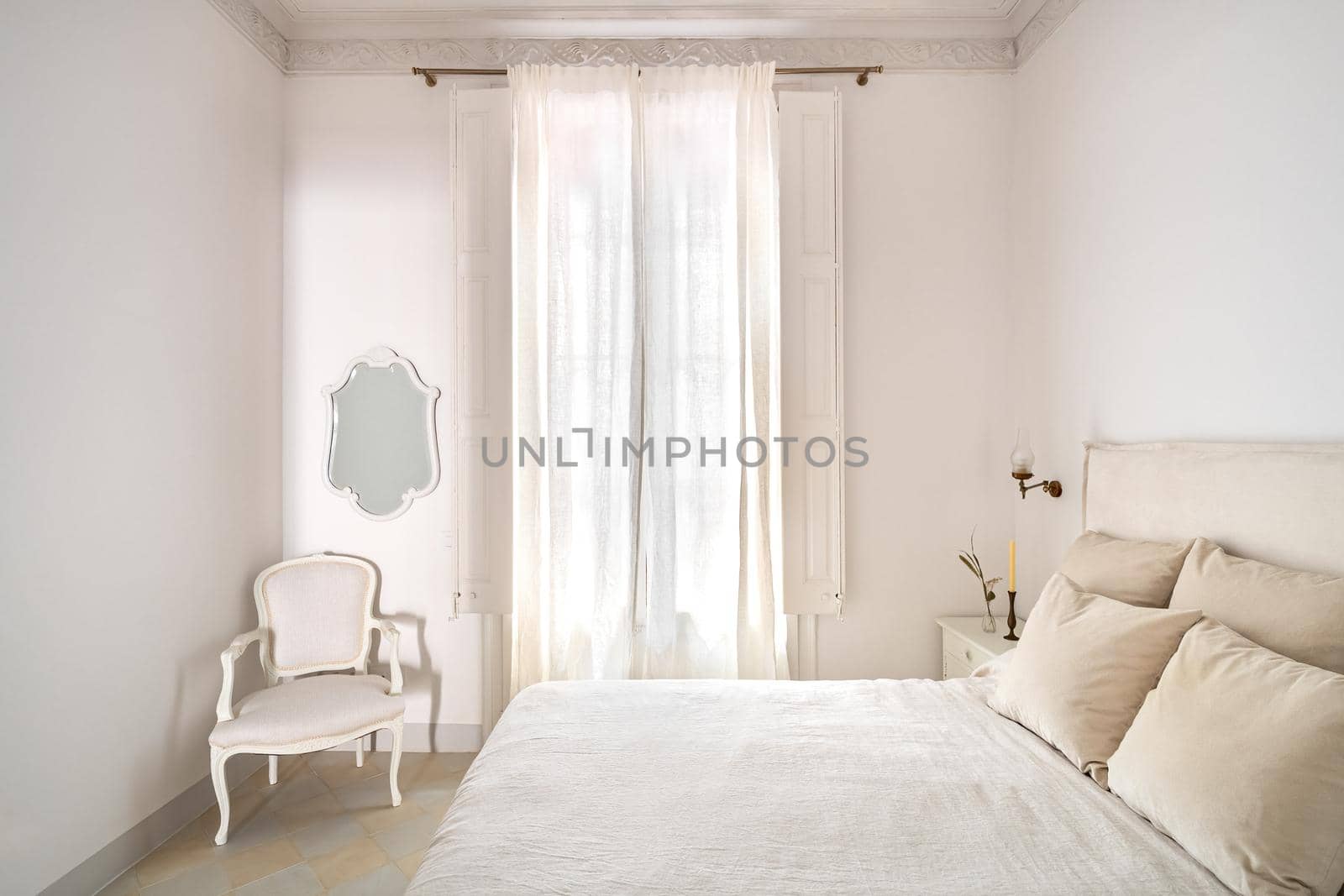 Bright bedroom interior, cozy bed with beige linen, dry flowers on a bedside table. Daylight shines through a window with a curtain