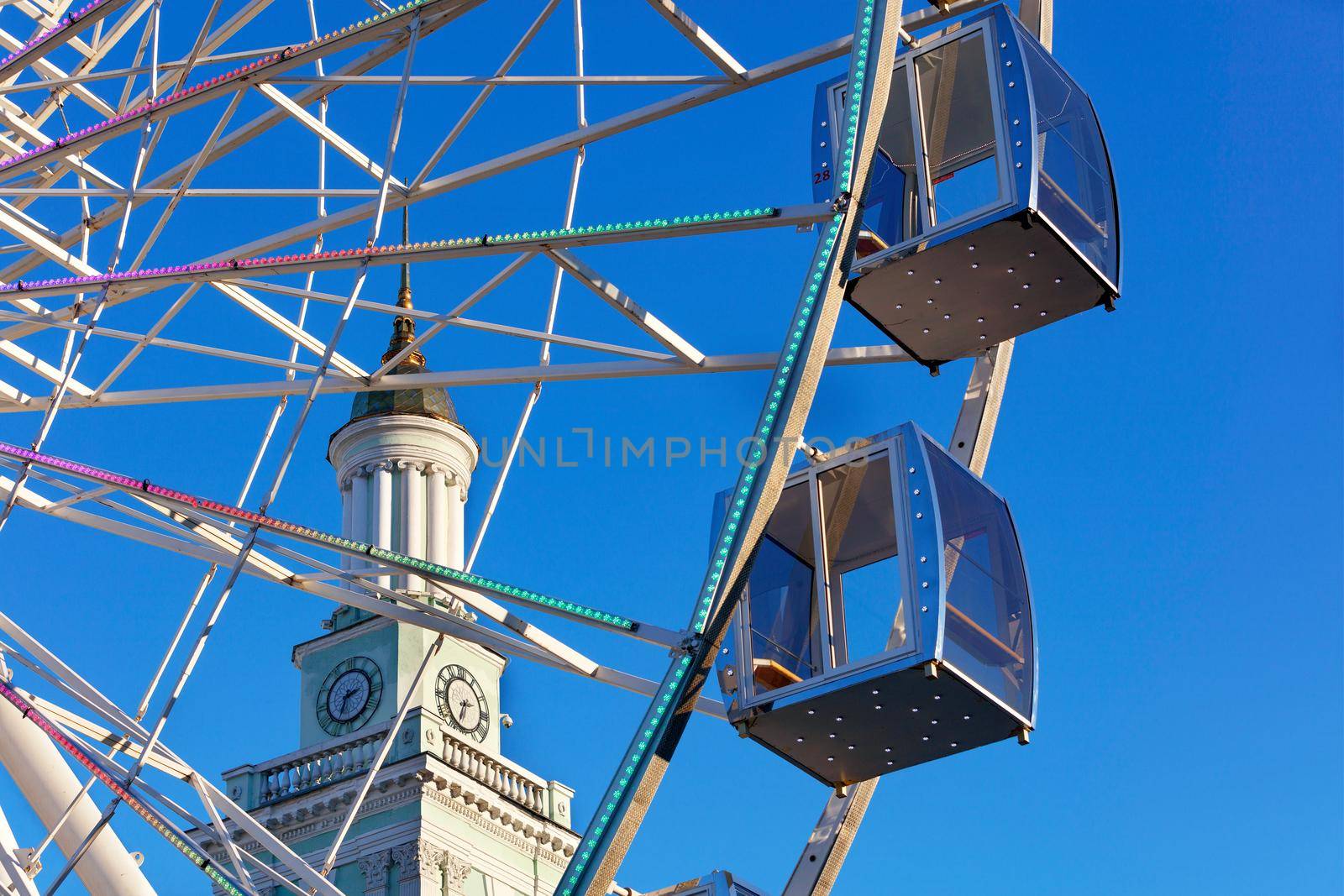 A beautiful and scenic view of the empty cabins of the Ferris wheel against the blue sky and the spire of the old clock tower in the afternoon.