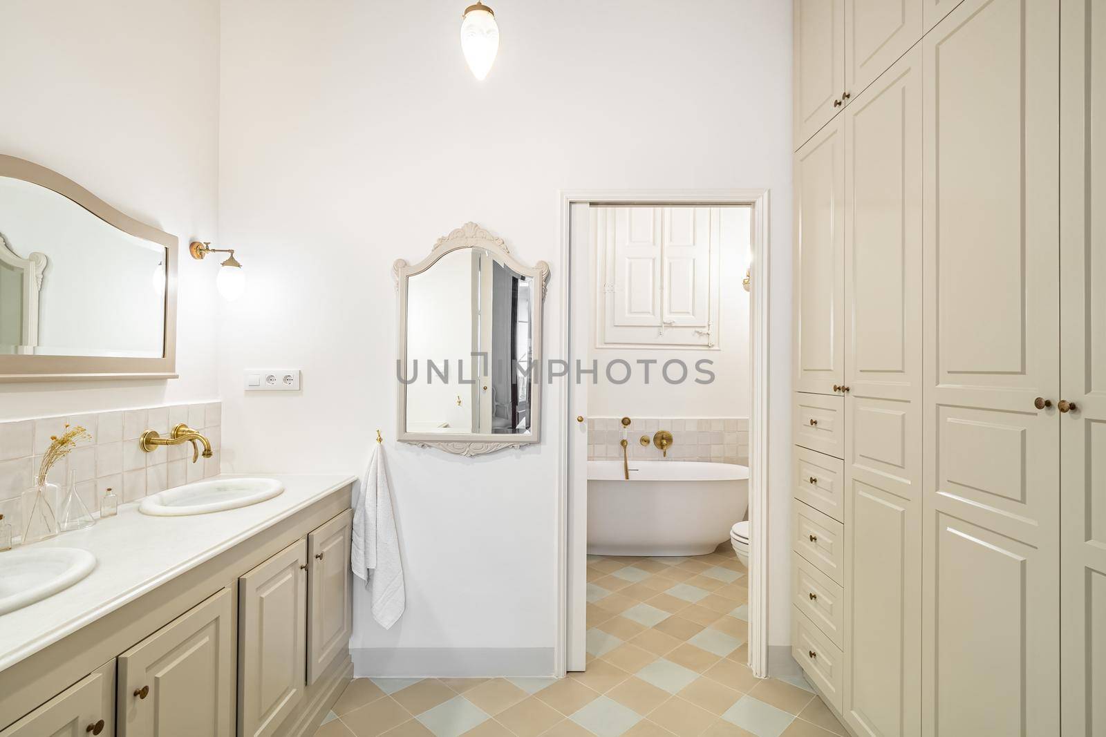 Interior of retro or classic style bathroom decorated in beige color with bath zone, big wardrobe, two sinks and vintage mirrors
